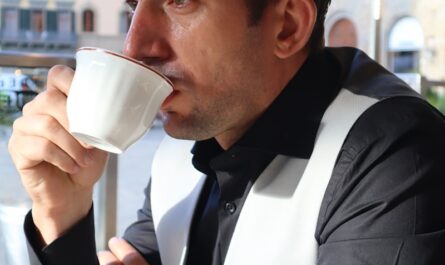 a man sitting at a table drinking a cup of coffee