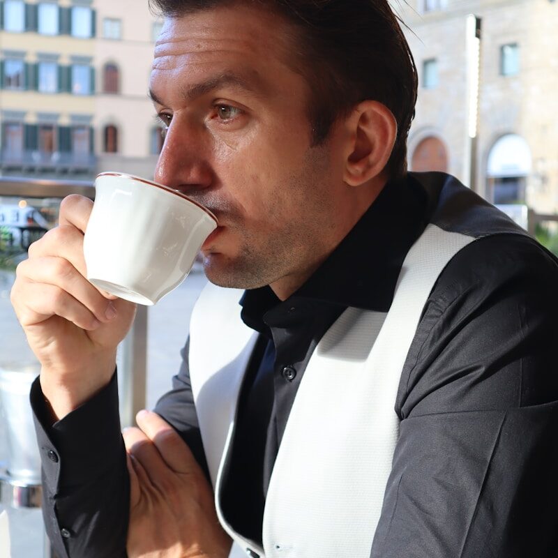 a man sitting at a table drinking a cup of coffee